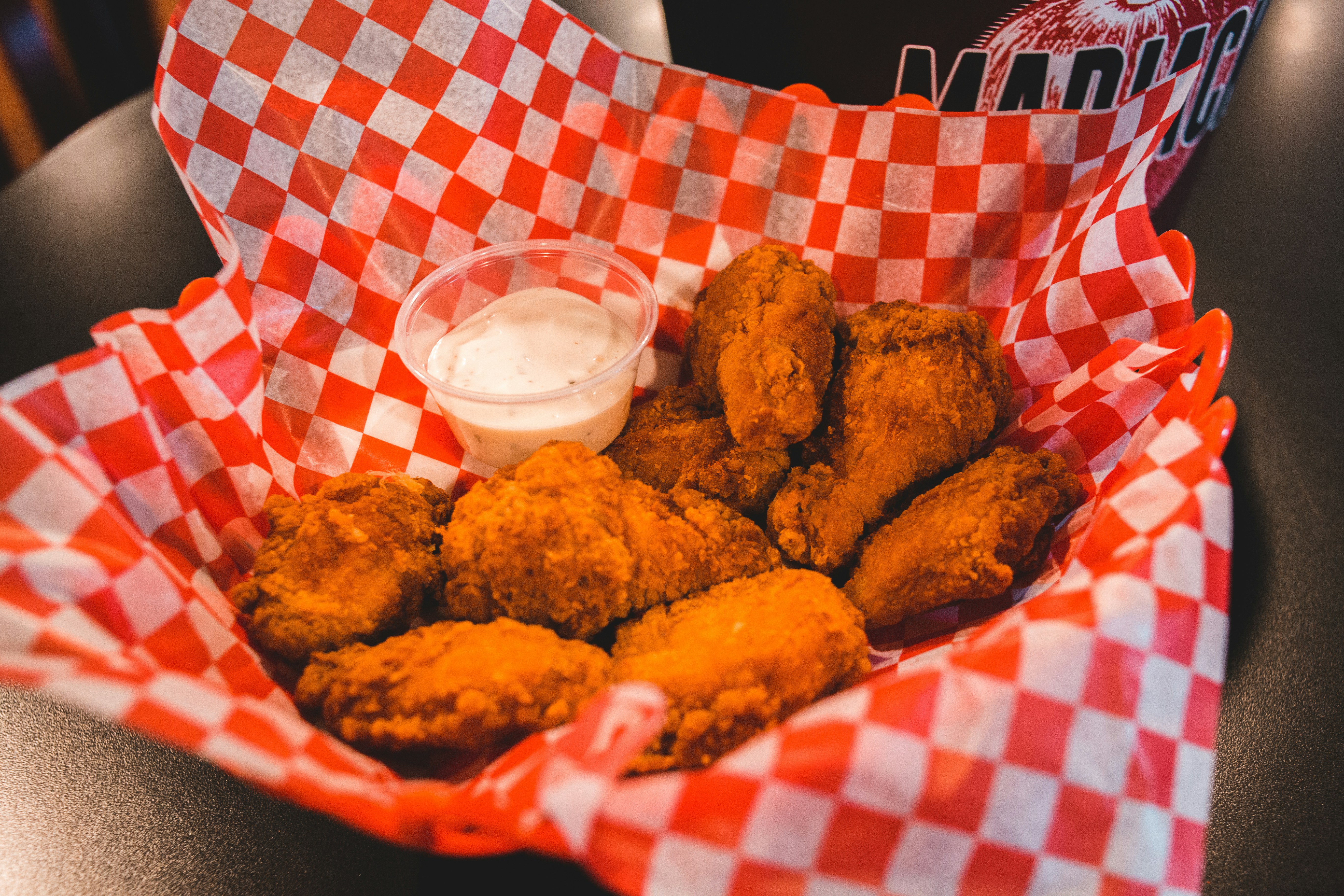A basket of crispy, spicy chicken wings with a container of ranch